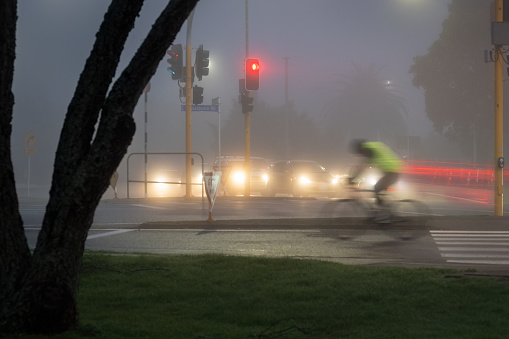 A cyclist riding in the morning fog. Cars stop at the traffic light. Motion blur image due to slow shutter speed.
