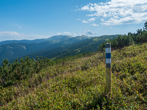 sign pole with tourist mark at ridge of Low Tatras mountains, hiking trail with mountain meadow, scrub pine and grassy green hills and slopes. Slovakia, summer sunny day, blue sky background