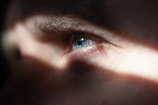 A man looking up only his blue eye is in the frame in close-up, illuminated by a sunbeam
