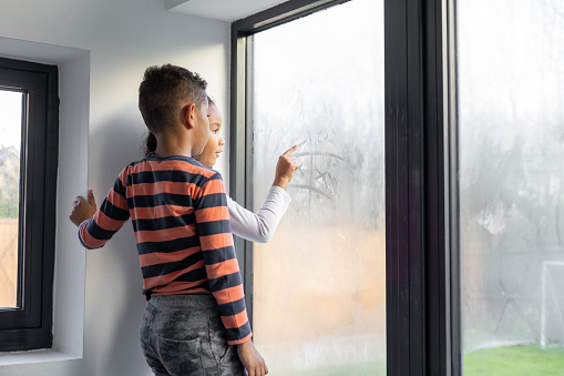 Brother and sister playing noughts and crosses on a steamed-up window. They are both wearing casual clothing.