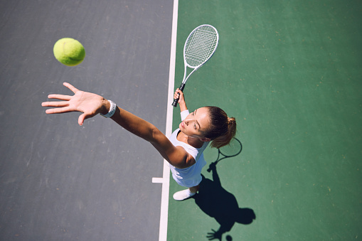 Fit tennis player, sport and serving during training, workout and exercise or match, game and competition from above. Sporty, active and healthy woman throwing a ball and practicing serve with racket