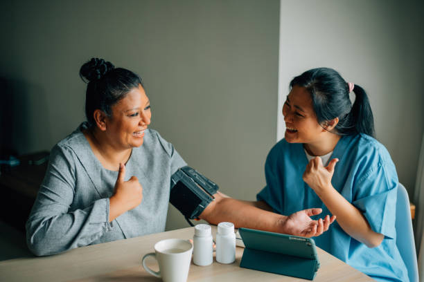 Healthcare worker taking blood pressure of senior woman at home stock photo