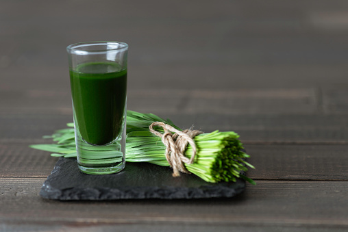 A bundle of wheatgrass with wheatgrass smoothie on wooden background.