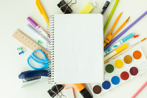 Blank notepad for free text next to the school supplies on the white background. Back to school concept on September day. Flat lay. Free space.
