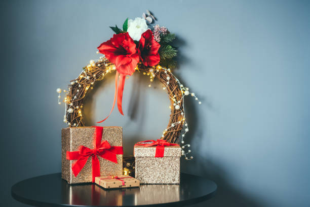 poucas caixas de presente douradas brilhantes com fita vermelha de veludo e elegante coroa de flores de natal na mesa preta no fundo da parede cinza. decoração de casa minimalista e festiva. estilo escandinavo. copie o espaço. - bow christmas red velvet - fotografias e filmes do acervo