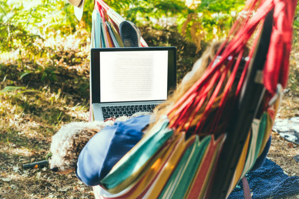 istock Back view woman working on laptop while lying in hammock, with her cockapoo puppy near motorhome on camping trip. Female living on camper car with animals and travel the world. Remote worker people. 1416910047