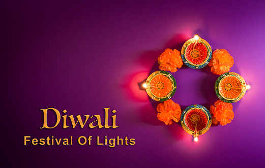 Happy Diwali - Clay Diya lamps lit during Dipavali, Hindu festival of lights celebration. Colorful traditional oil lamp diya on purple background