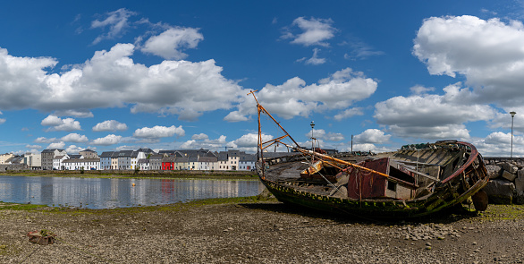 Galway, Ireland - 28 July, 2022: old shipwreck on the banks of the River Corrib with the colorful houses of the Long Walk in downtwon Galway
