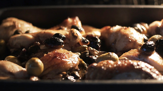 Tray filled with chicken breasts inside oven. Close up of chicken being baked in the oven with olives, spices, garlic and vegetable oil, food and cooking concept.