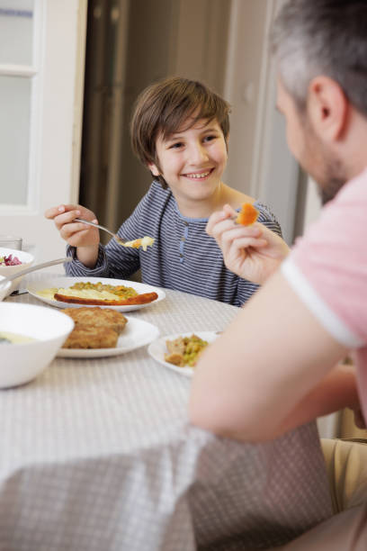 istock Smiling boy sitting at the dining table, looking at his father and having lunch 1416913371