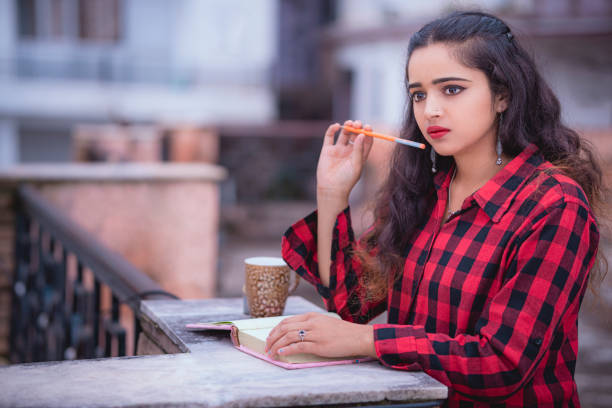 An Asian/Indian adult female student studies and contemplates on a rooftop of her apartment in this day image with copy space.