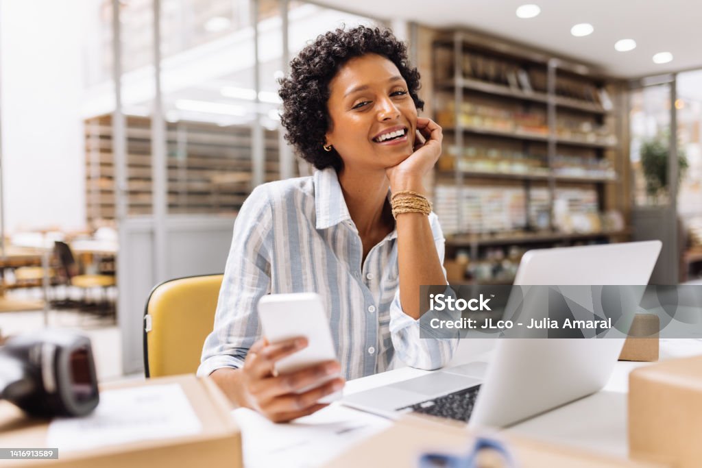 Successful online store owner smiling at the camera in a warehouse Successful online store owner smiling at the camera while working in a warehouse. Happy female entrepreneur managing online orders on her website. Businesswoman running an e-commerce small business. Happiness Stock Photo
