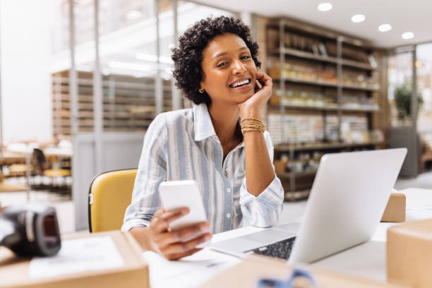 Successful online store owner smiling at the camera in a warehouse Successful online store owner smiling at the camera while working in a warehouse. Happy female entrepreneur managing online orders on her website. Businesswoman running an e-commerce small business. warehouse office stock pictures, royalty-free photos & images