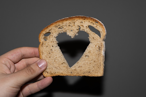 Rye bread bread slice with heart shaped hole on a hand grey