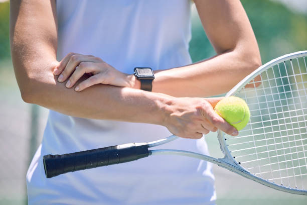 sport-, aktiv- und tennisspieler mit schläger und ball, der auf einem spielbereiten platz steht. nahaufnahme eines fitten, starken und professionellen mannes mit ausrüstung, der eine verletzung an seinem arm berührt. - ellenbogen stock-fotos und bilder