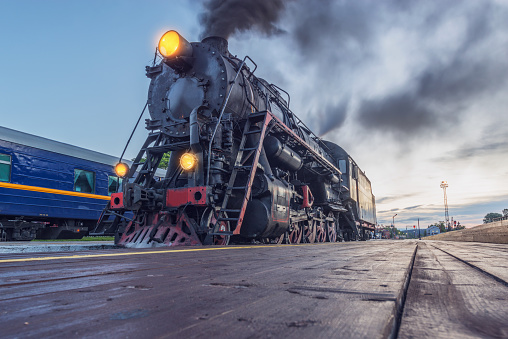 Steam locomotive stands by the wooden station platform at sunrise.