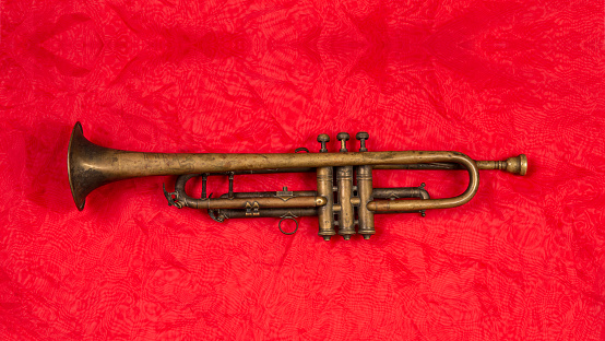 Old golden trumpet on shiny red fabric isolated.