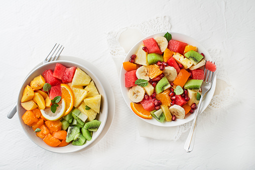 Bowls of fresh mixed fruit salad on white background, top view