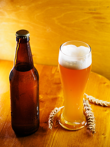 A glass of cold wheat beer and a bottle of beer on a wooden table