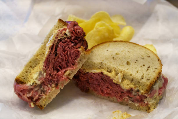 Massive pastrami sandwich with mustard and chips on white paper