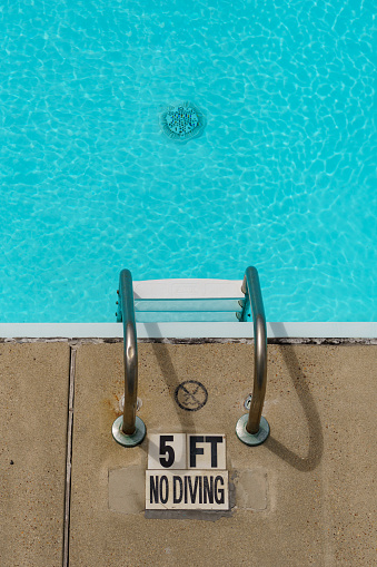 No diving sign by a pool ladder. The water is clear and blue, and you can see the pool drain. Water depth is marked as 5 feet.