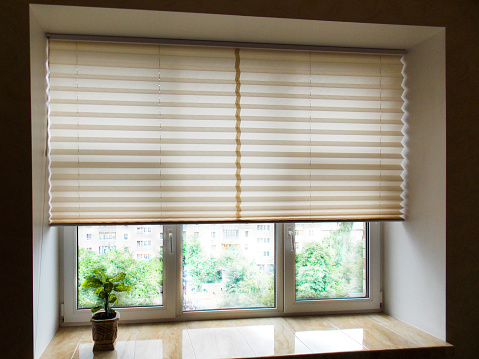 Pleated blinds XL, beige color, with 50mm fold closeup in the window opening in the interior. Home blinds - modern bottom up privacy shades half raised on apartment windows.