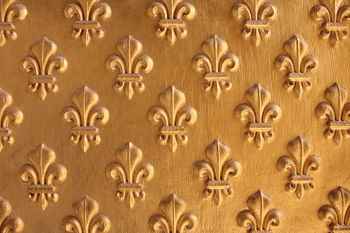 Fleur de Lis pattern painted gold over wooden texture for background. Repeated fleur-de-lis pattern.