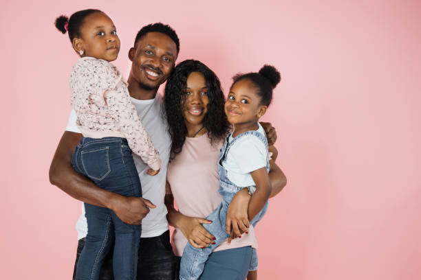 istock Happy african parents and two daughters embracing each other standing over pink studio background 1416943707