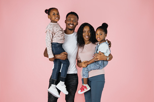 Loving family. Happy african parents and two daughters embracing each other standing over pink studio background, copy space.