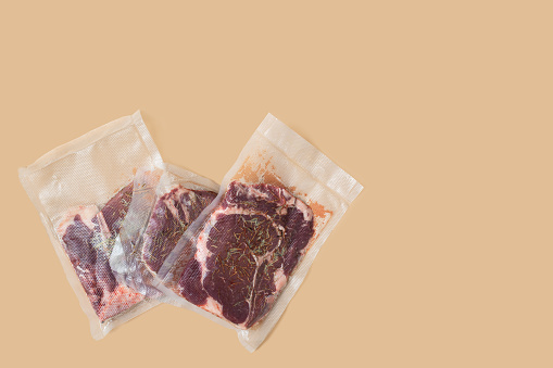 Raw fresh vacuum-packed meat for sous-vide. T-bone steak on beige background
