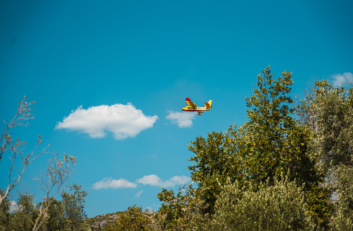 Dubrovnik, Croatia - July 31, 2022: Canadair CL-415 flying over a small village Orašac, a few km from Dubrovnik, Croatia. Four planes were in action and flying around all day, to put out the fire near there. Canadair plane can take a huge amount of water from the sea or a lake and release it over the fire.