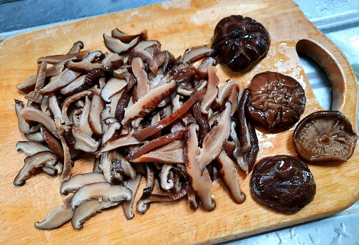 Slicing Shiitake mushrooms on cutting board - food preparation.
