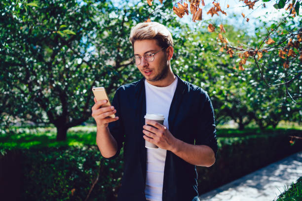 istock Guy with takeaway beverage browsing smartphone in park 1416947144