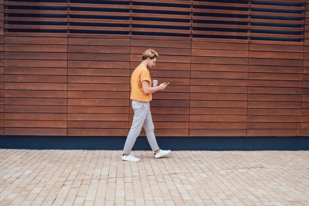 istock Male watching smartphone while walking against city wall 1416947150