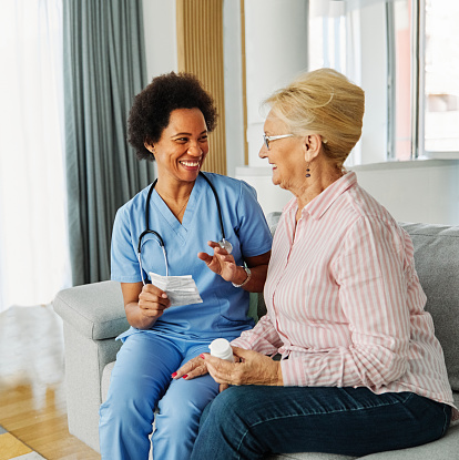 Doctor or nurse caregiver showing a prescription drug bottle to senior woman at home or nursing home
