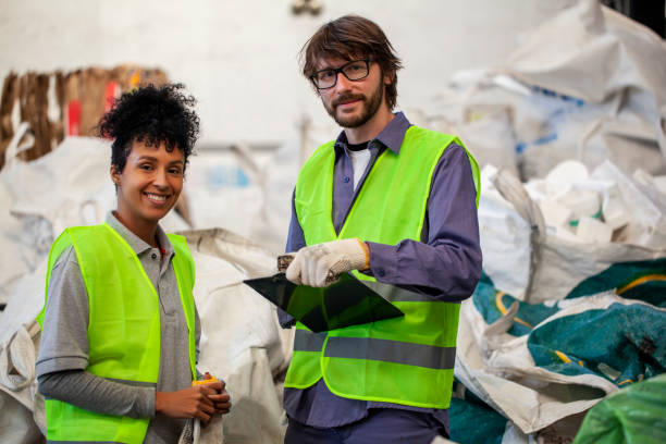 Portrait of mid adult colleagues holding clipboard while standing inside recycling centre stock photo