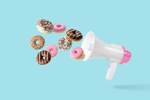 Colorful donuts with White-Pink megaphone on a pastel blue background. Creative minimal food concept.