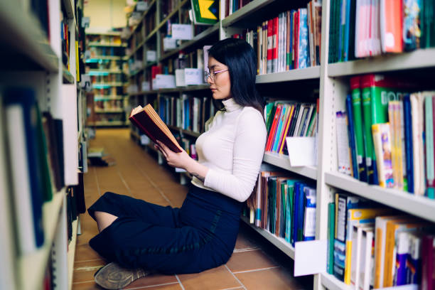 istock Dark haired woman reading book in library 1416953135