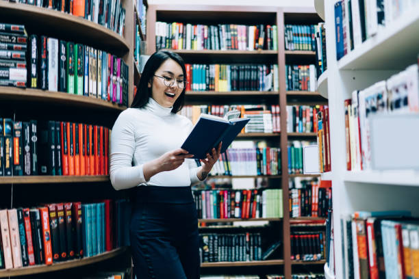 istock Cheerful young woman reading book in college library 1416953432
