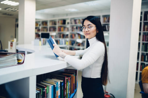 istock Young woman holding book in library 1416953485