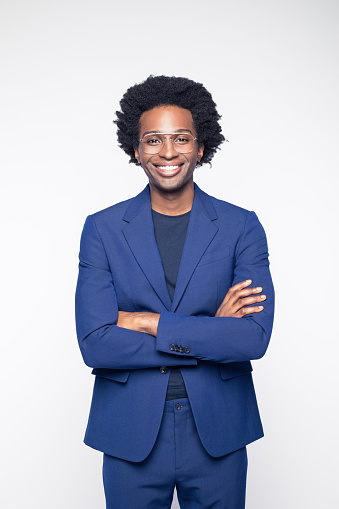 Portrait of happy businessman wearing navy blue suit standing with arms crossed and smiling at camera. Studio shot against white background.