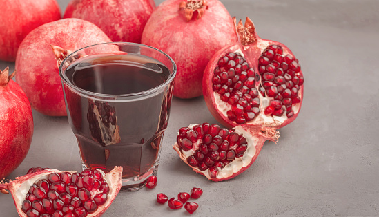 Fresh pomegranate juice in a glass and a lot of pomegranates on a gray concrete surface. Copy space.