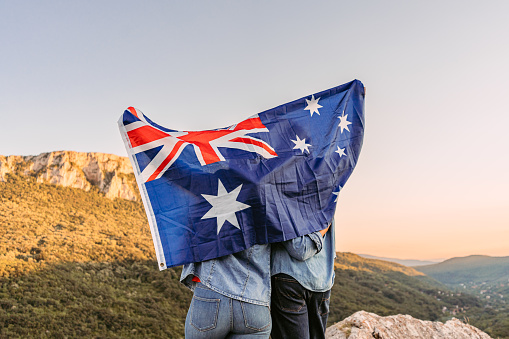 Beautiful young happy couple waving an Australian flag at the top of the mountain.