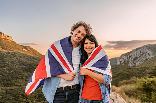 Beautiful young happy couple wrapped in a Great Britain flag at the top of the mountain.