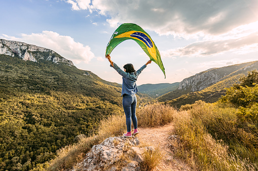Beautiful young woman waving a Brazilian flag at the top of the mountain.