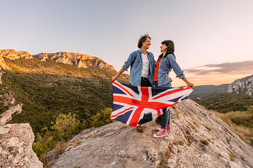 Beautiful young happy couple waving a Great Britain flag at the top of the mountain.