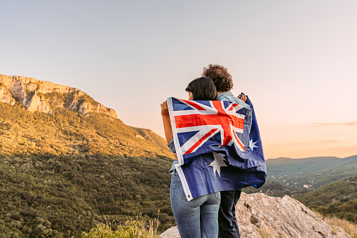 Beautiful young happy couple wrapped in an Australian flag at the top of the mountain.
