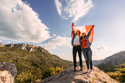 Beautiful young happy couple waving a Canadian flag at the top of the mountain.