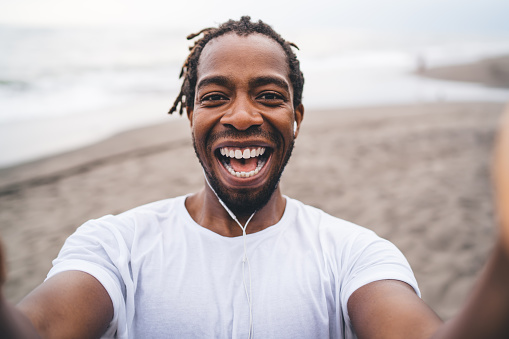 Laughing black man holding camera and taking selfie on seacoast