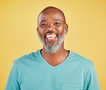 Mature african man laughing out loud against a yellow studio background. Black guy giggling and reacting with laughter while looking cheerful and happy. Lighten the mood with an amusing and funny joke